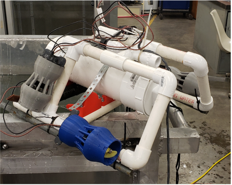 PVC pipe frame with wiring and two underwater thrusters mounted on a metal test tank in a workshop.