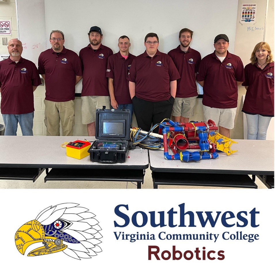 Group of students and instructors in matching maroon shirts stand behind a table with robotics equipment and a robot prototype; Southwest Virginia Community College Robotics logo below.