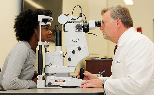 Optometrist performing an eye exam for a patient using a slit-lamp microscope.