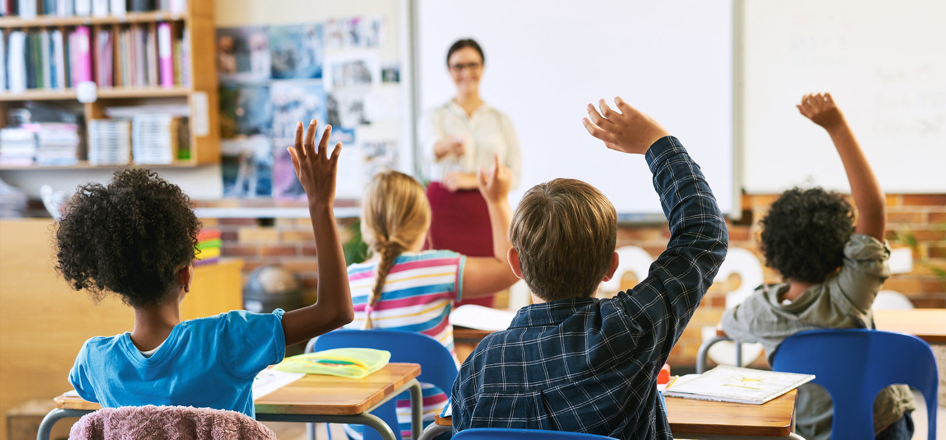 students raising their hand in a classroom with a teacher in the front