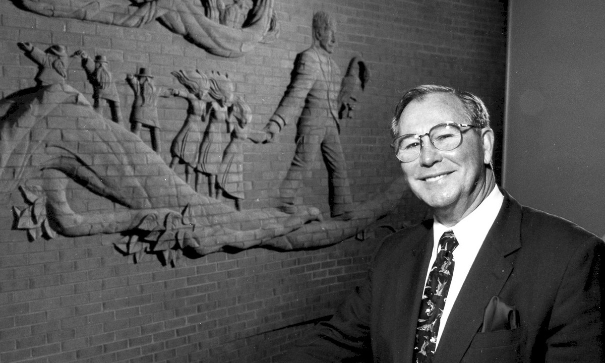 Dr. Charles R. King standing in front of the Jack Tales Wall, a brick sculpture in the building bearing his name.